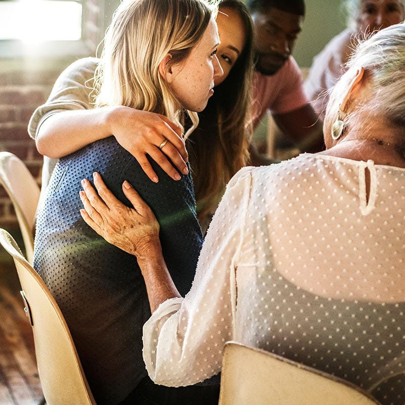 a group of people put their arms around a group member struggling in an outpatient addiction program