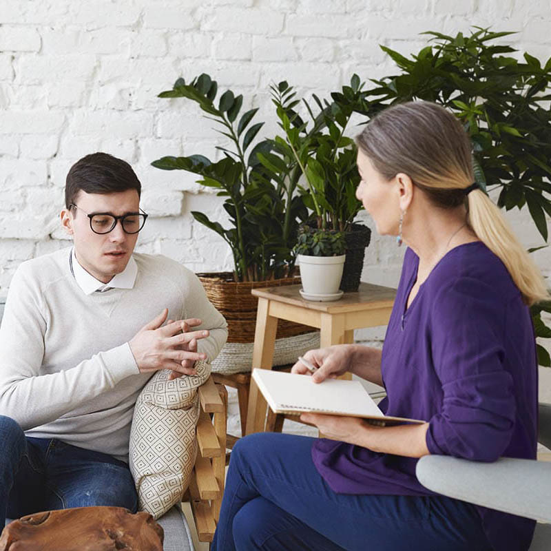 a patient talks to a therapist while they both sit in chairs and talk about an outpatient alcohol treatment center