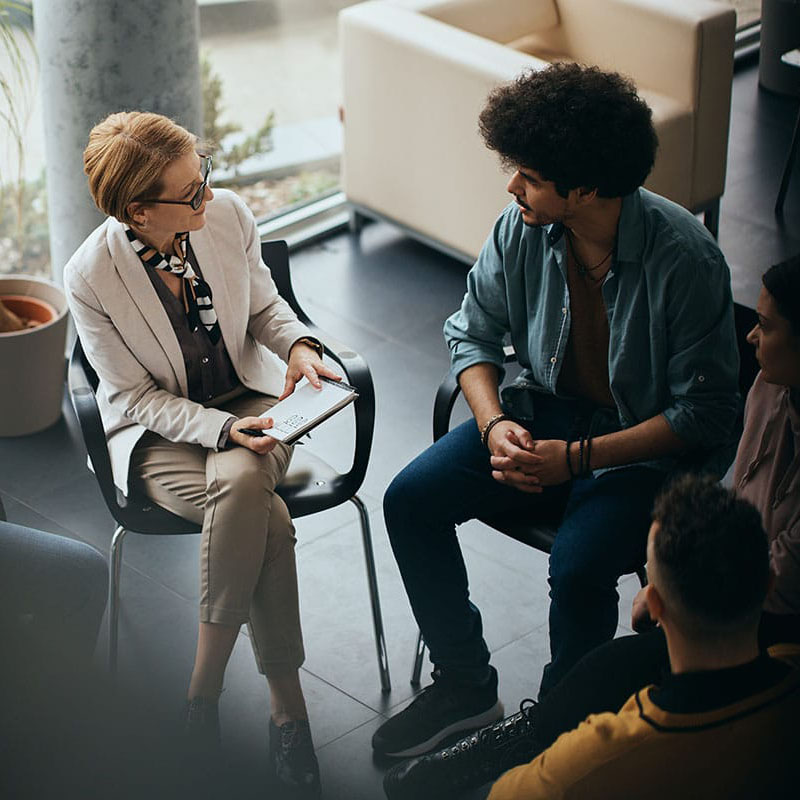 a group of people talk to a therapist while sitting in chairs and participating in an outpatient drug treatment program