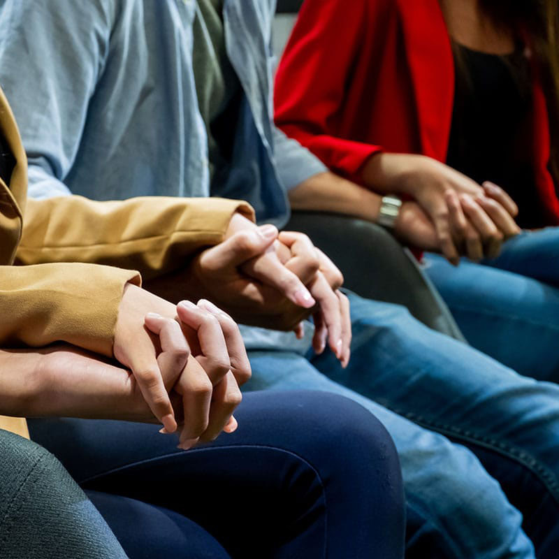 a line of people hold hands to participate in a group therapy session in outpatient treatment