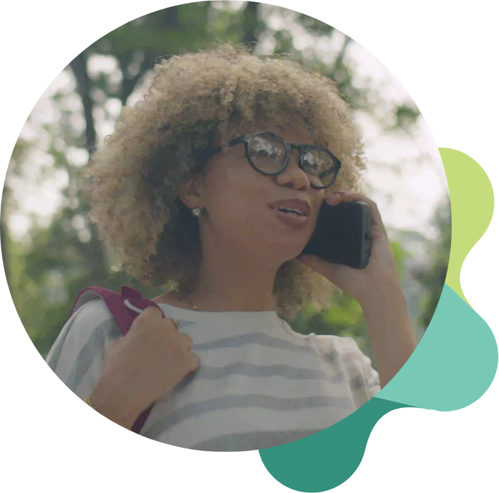 a woman with curly hair and glasses talks on the phone, this image is in a circle with part of the Sanative Recovery and Wellness logo behind it