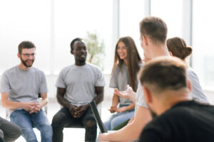 a group of people sit in a circle talking in a group therapy program