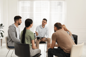 a group of people sit in a circle and talk in an opiate addiction treatment program
